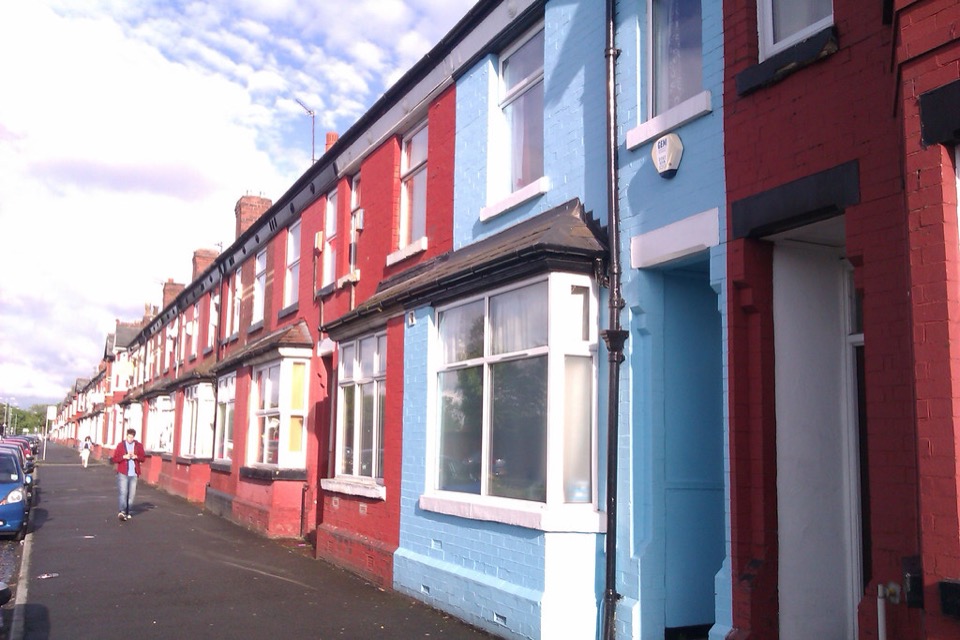 A row of terraced houses painted red and blue on a street in Manchester